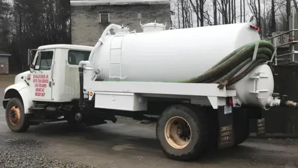 White septic truck parked outdoors next to a building.