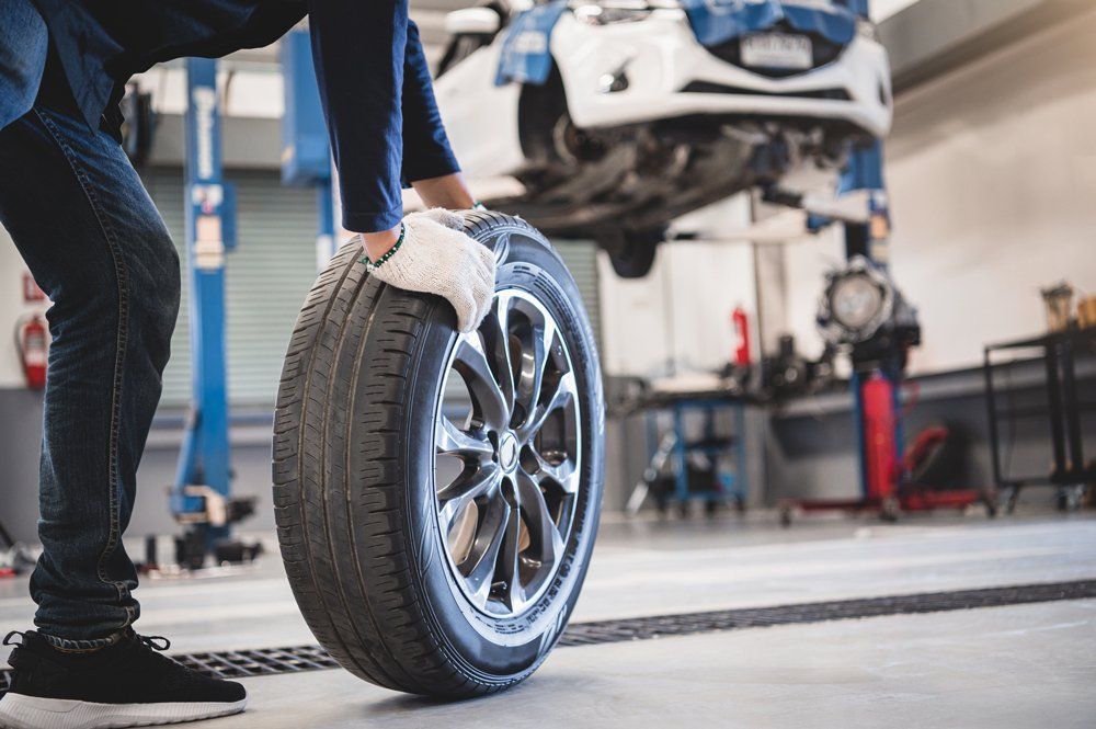 Male Mechanic Hold and Rolling Tire — Burgaw, NC — Thompson Enterprise of Burgaw