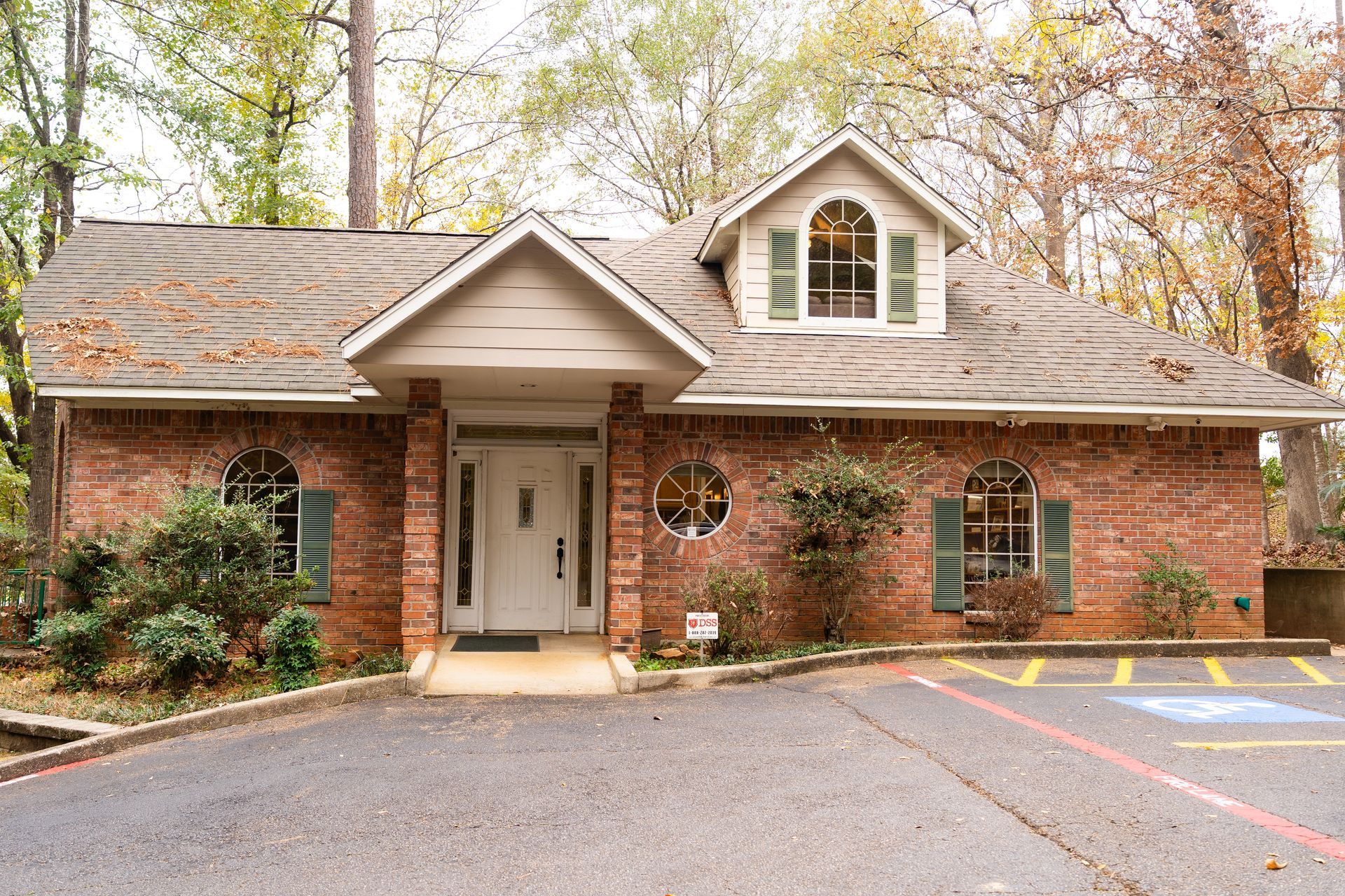 A single-story brick building with a white front entrance, dormer window, and an accessible parking spot in front.