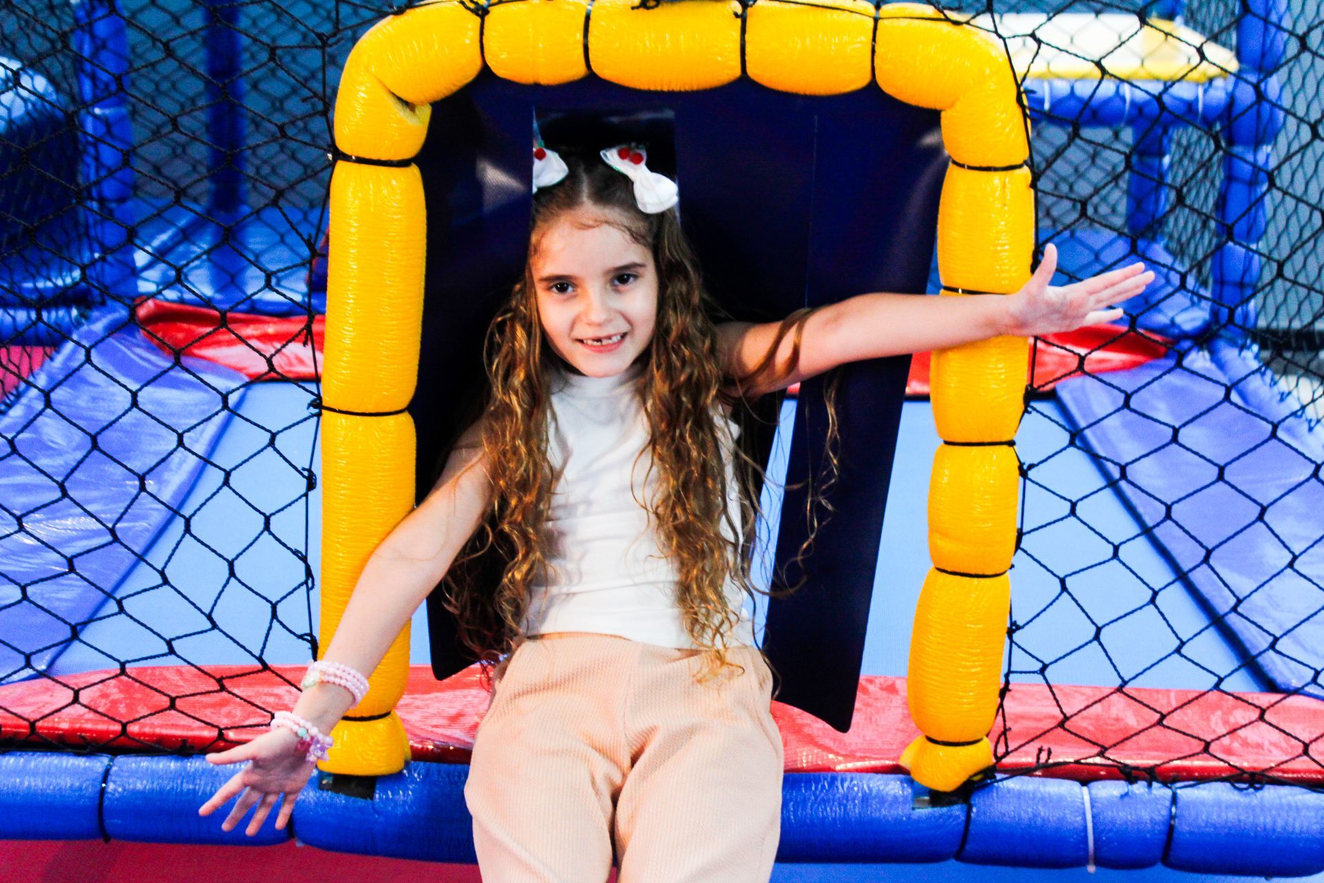 Menina com os braços estendidos em um arco acolchoado amarelo em um parque infantil coberto.