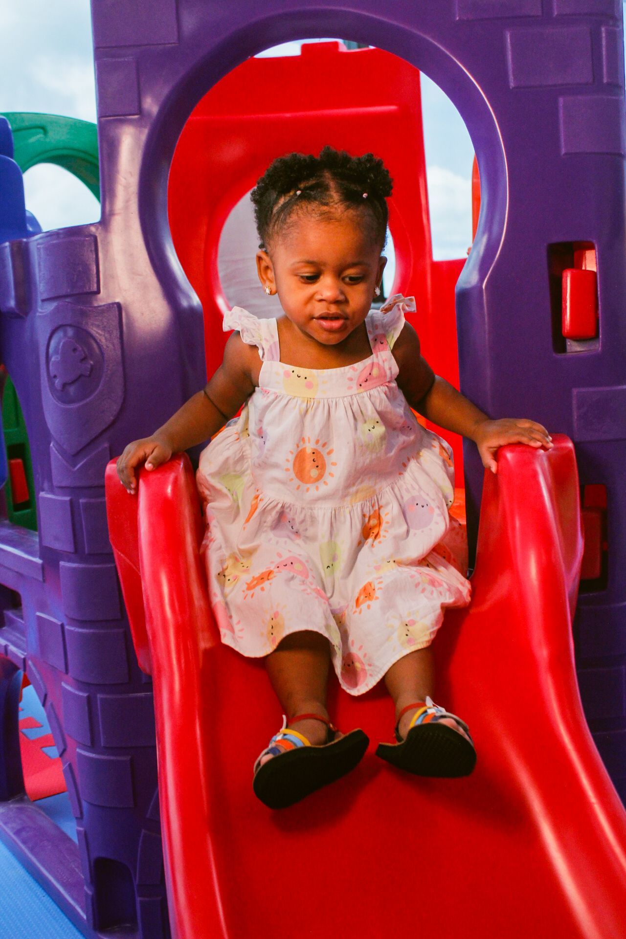 Criança deslizando por um escorregador vermelho em um parque infantil colorido.
