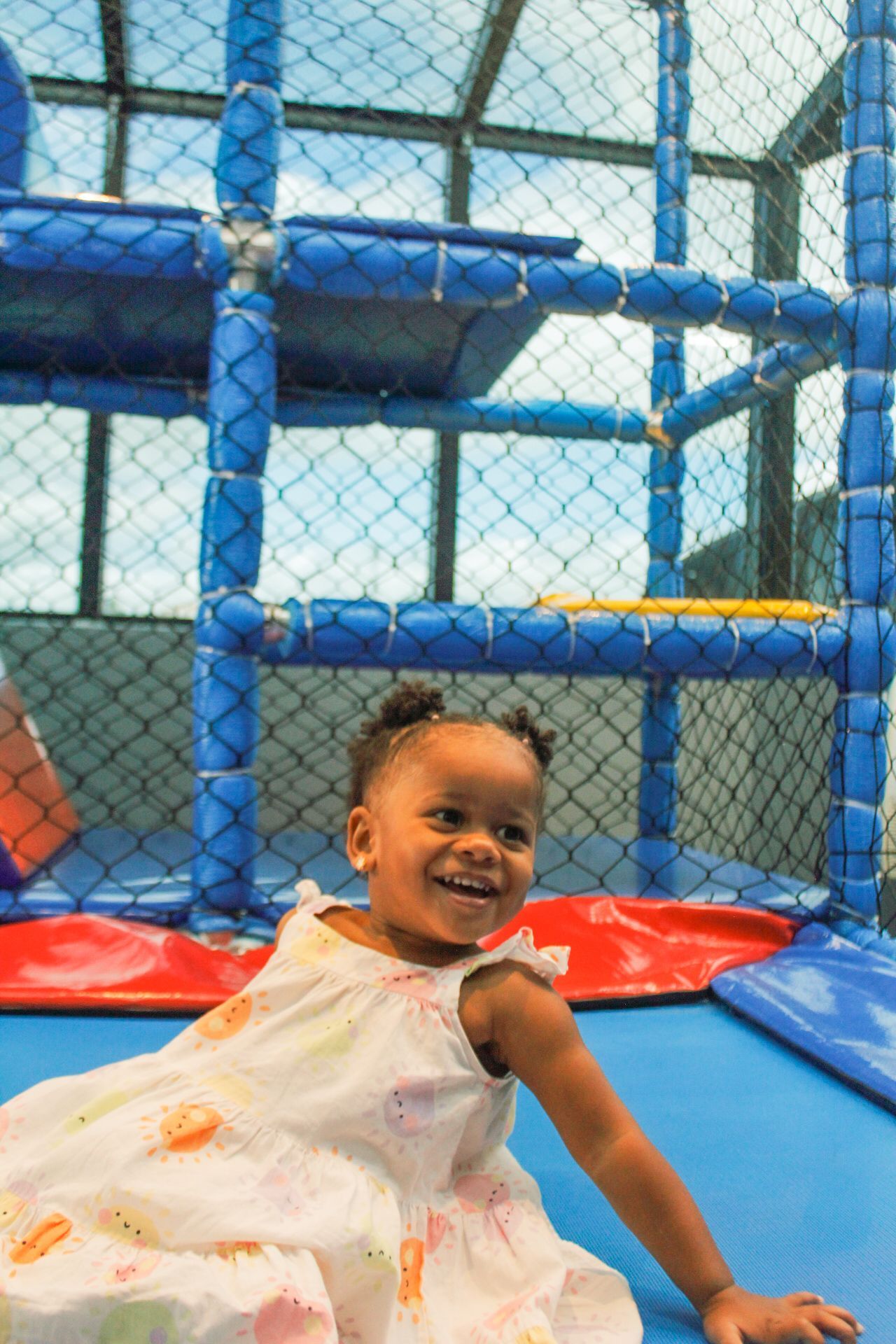 Criança sorridente de vestido branco em um brinquedo azul com janelas de tela.