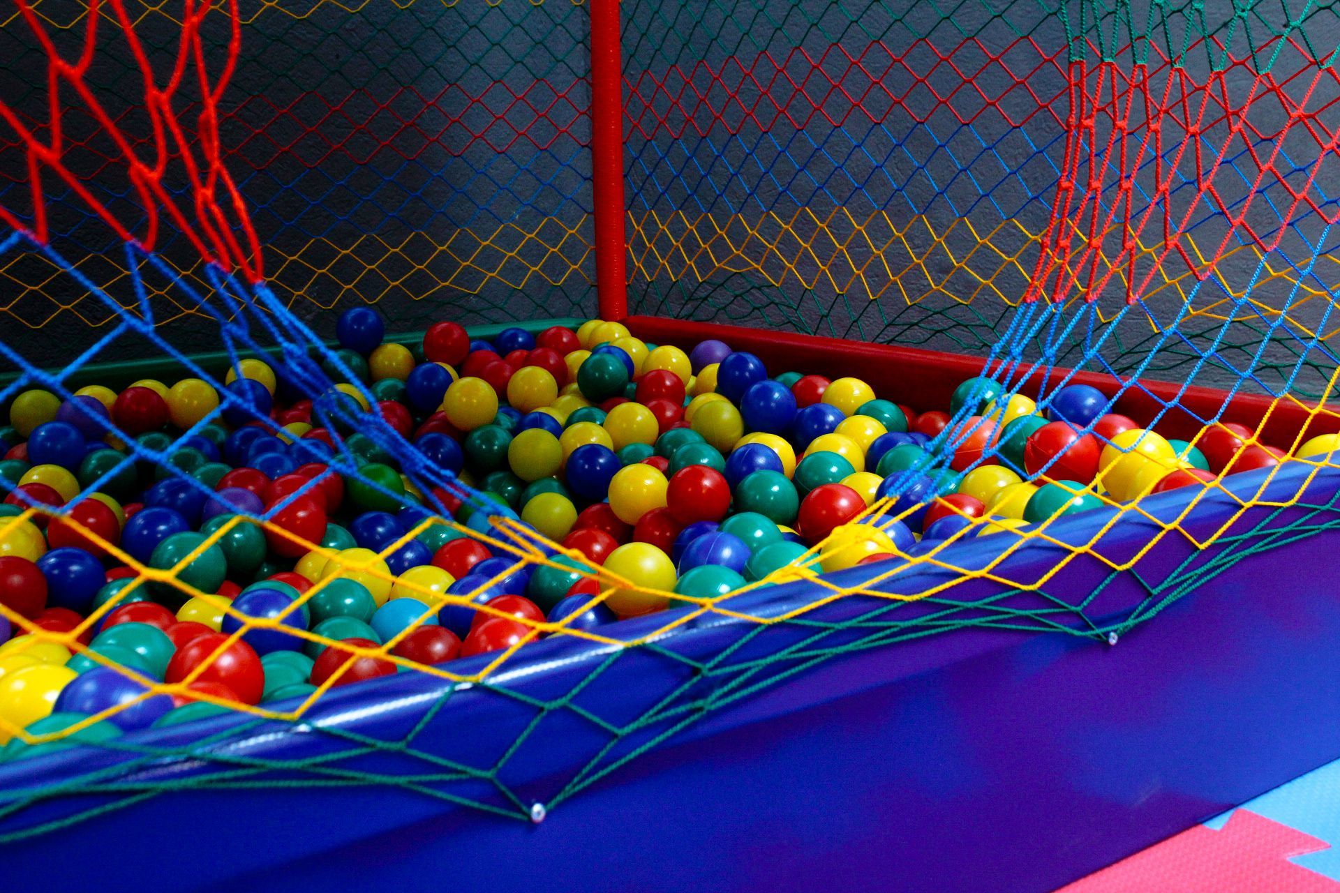 Uma piscina de bolinhas colorida com uma rede de proteção; as bolinhas são amarelas, azuis, verdes e vermelhas.