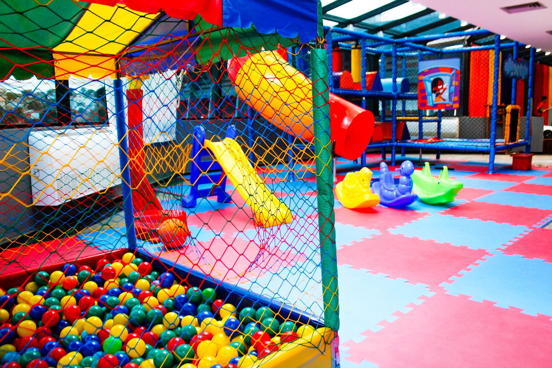 Área de lazer com piscina de bolinhas, escorregadores e piso colorido.