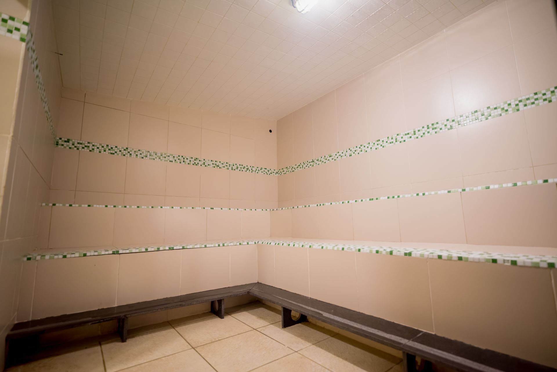 Vestiário vazio com paredes revestidas de azulejos, bancos e prateleiras, com detalhes em verde.