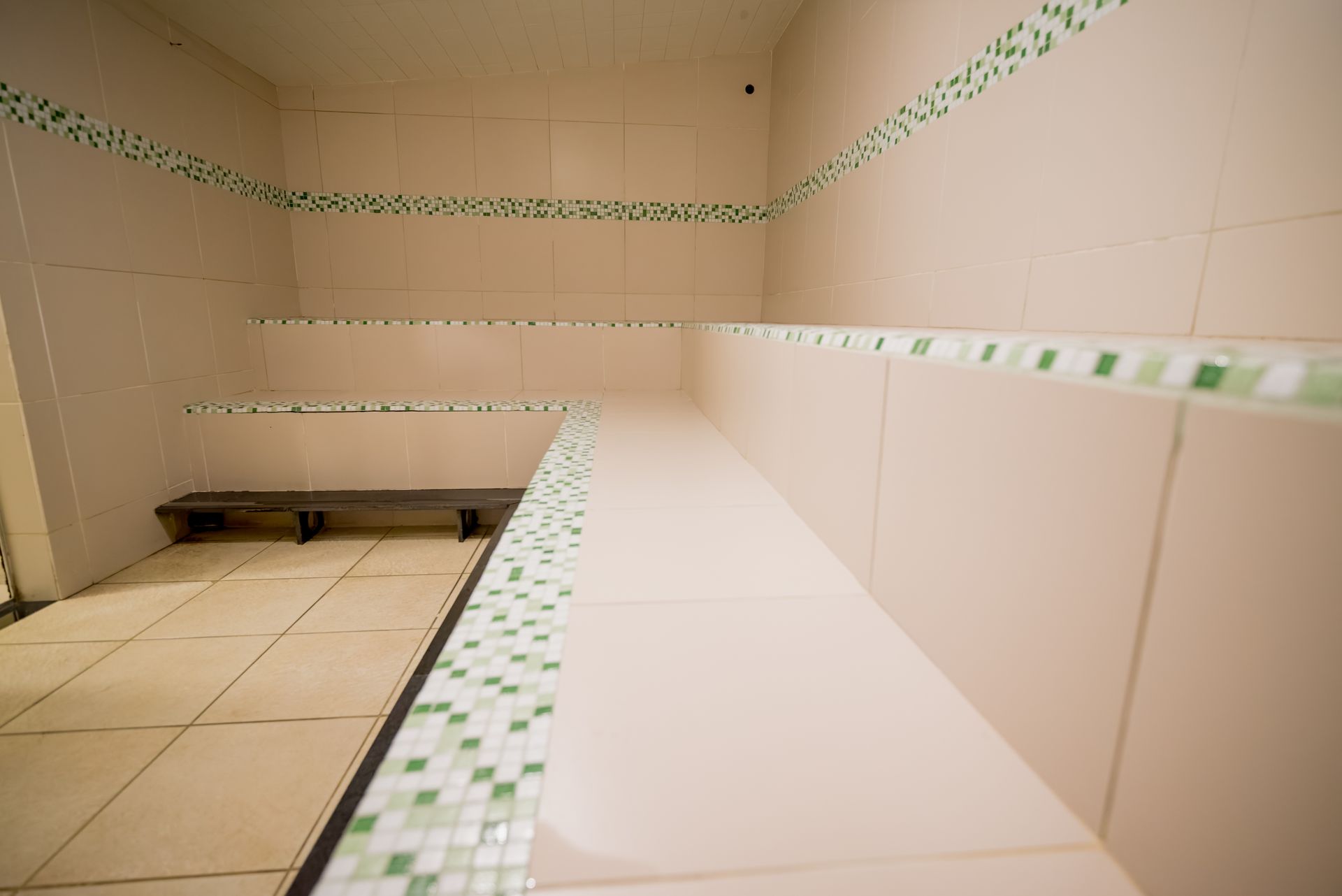 Sala de vapor vazia com paredes revestidas de azulejos, bancos e detalhes em azulejo verde.