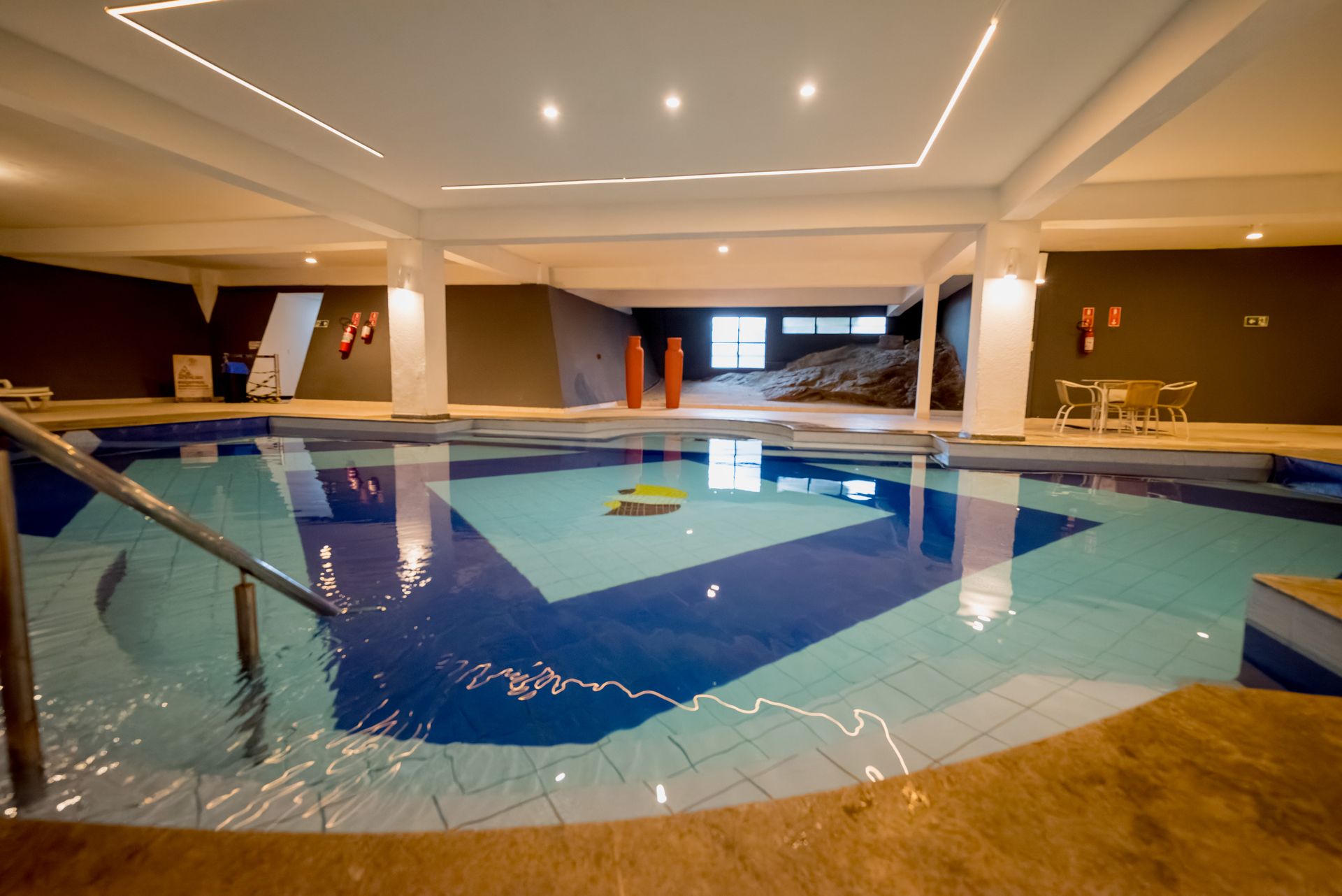 Piscina coberta com design em azulejos azuis e brancos, corrimão e área de estar.