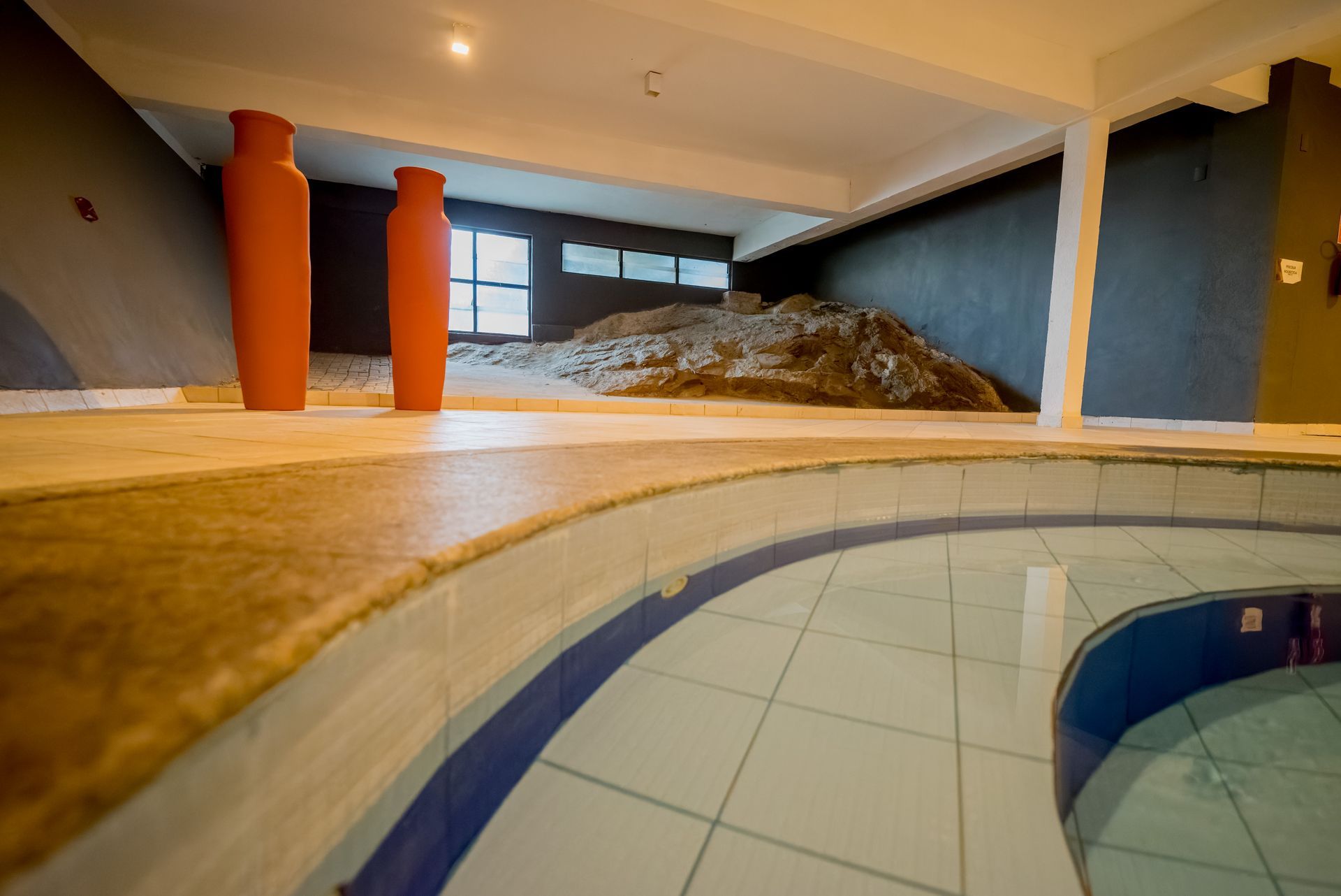 Área de spa interna com piscina, vasos de terracota e uma formação rochosa.