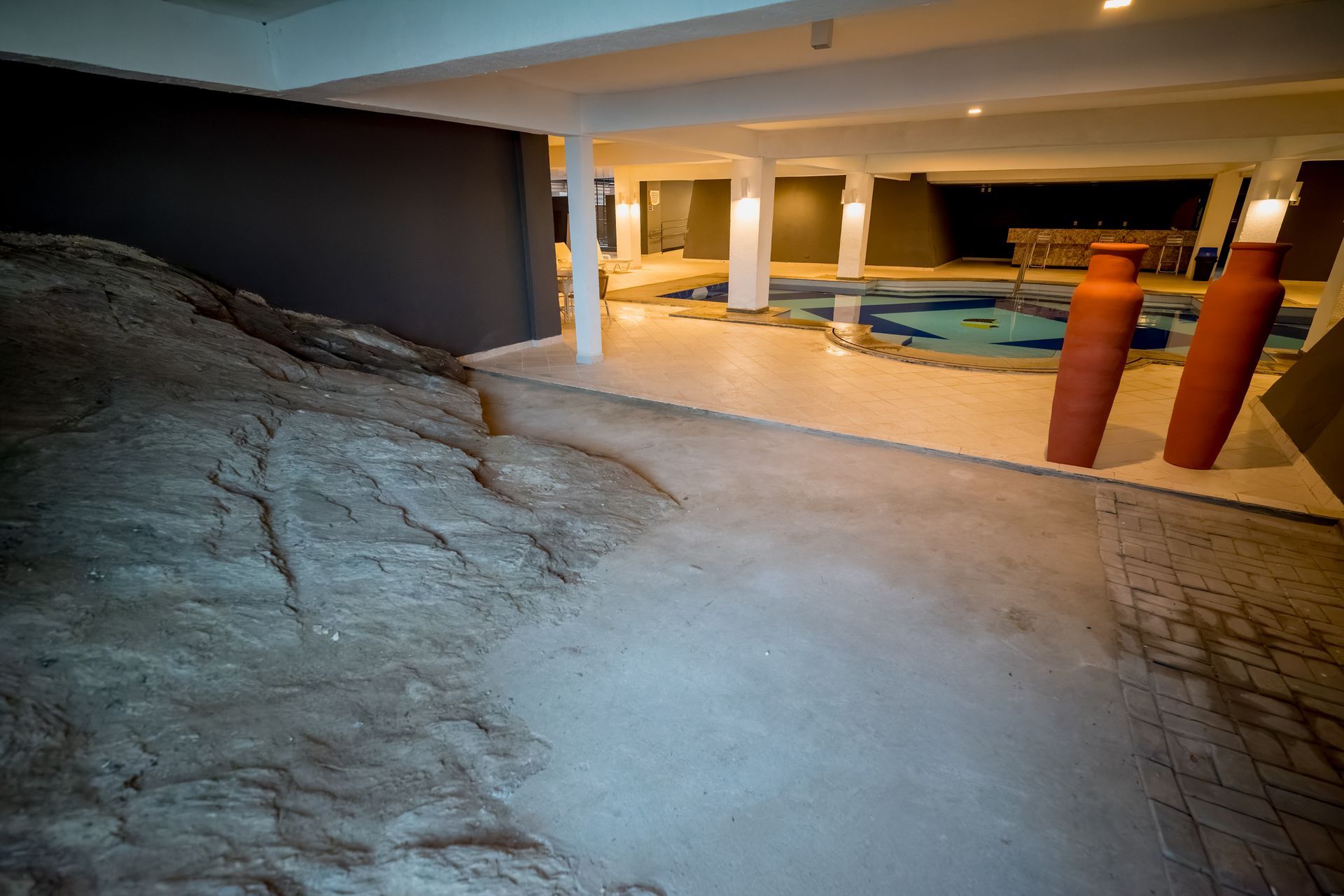 Spa interno com formações rochosas, piscinas, pilares e vasos de terracota.