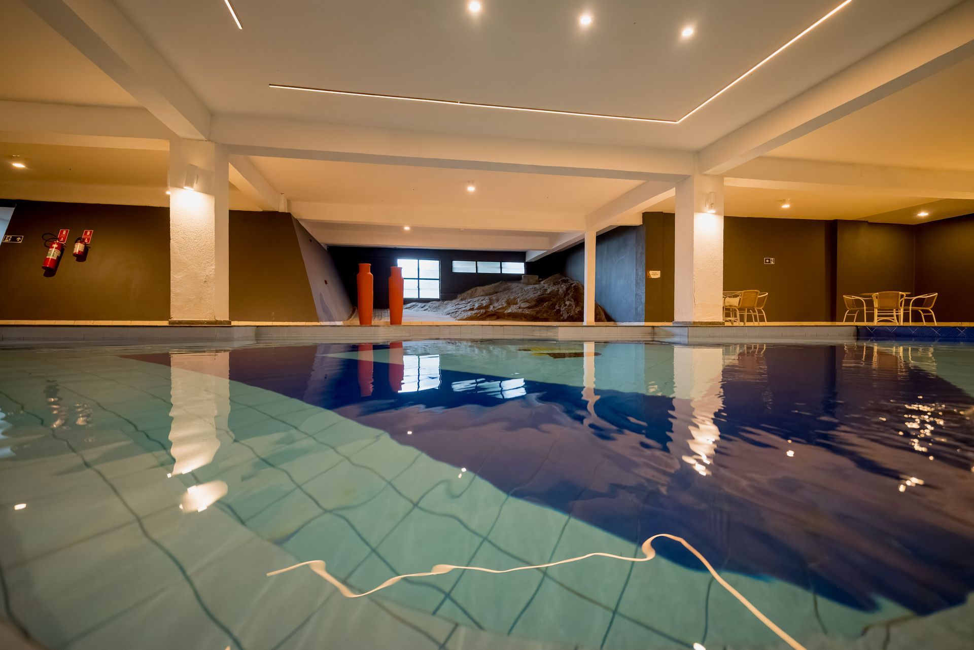 Piscina coberta com água que reflete as luzes do teto e as paredes escuras.