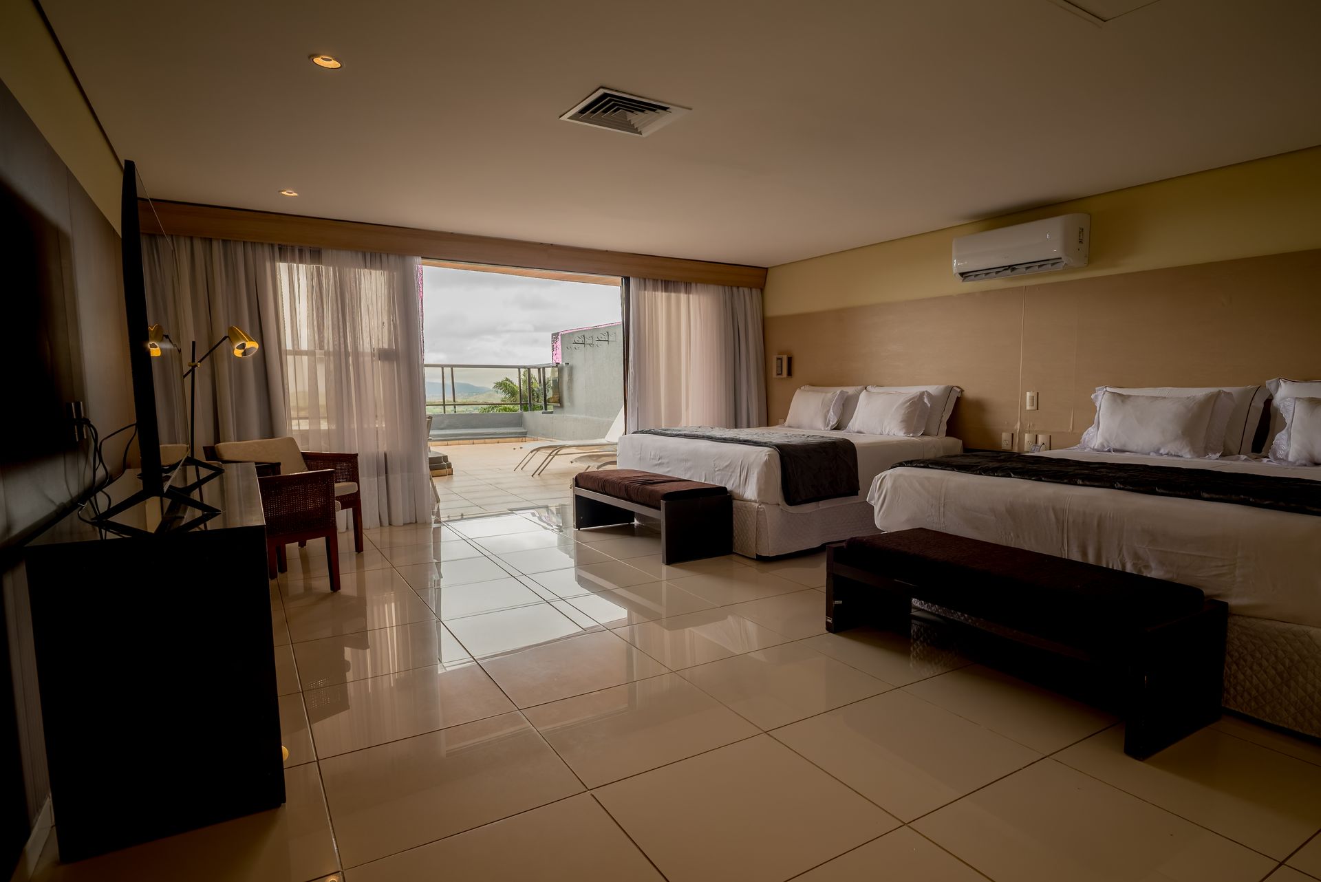 Um quarto de hotel com duas camas, uma escrivaninha, uma televisão e uma varanda.