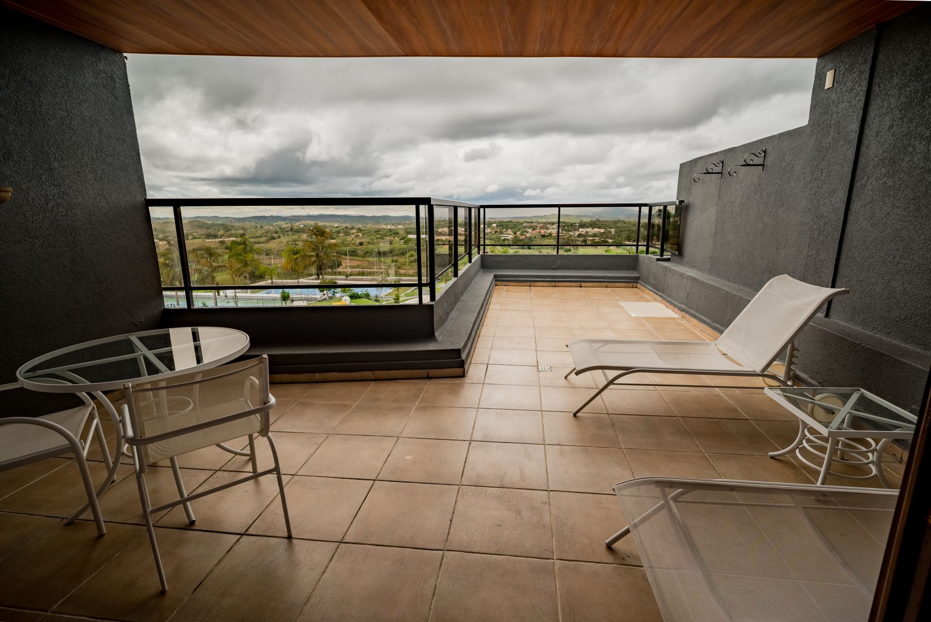 Uma varanda com cadeiras, uma mesa e vista para um céu nublado.