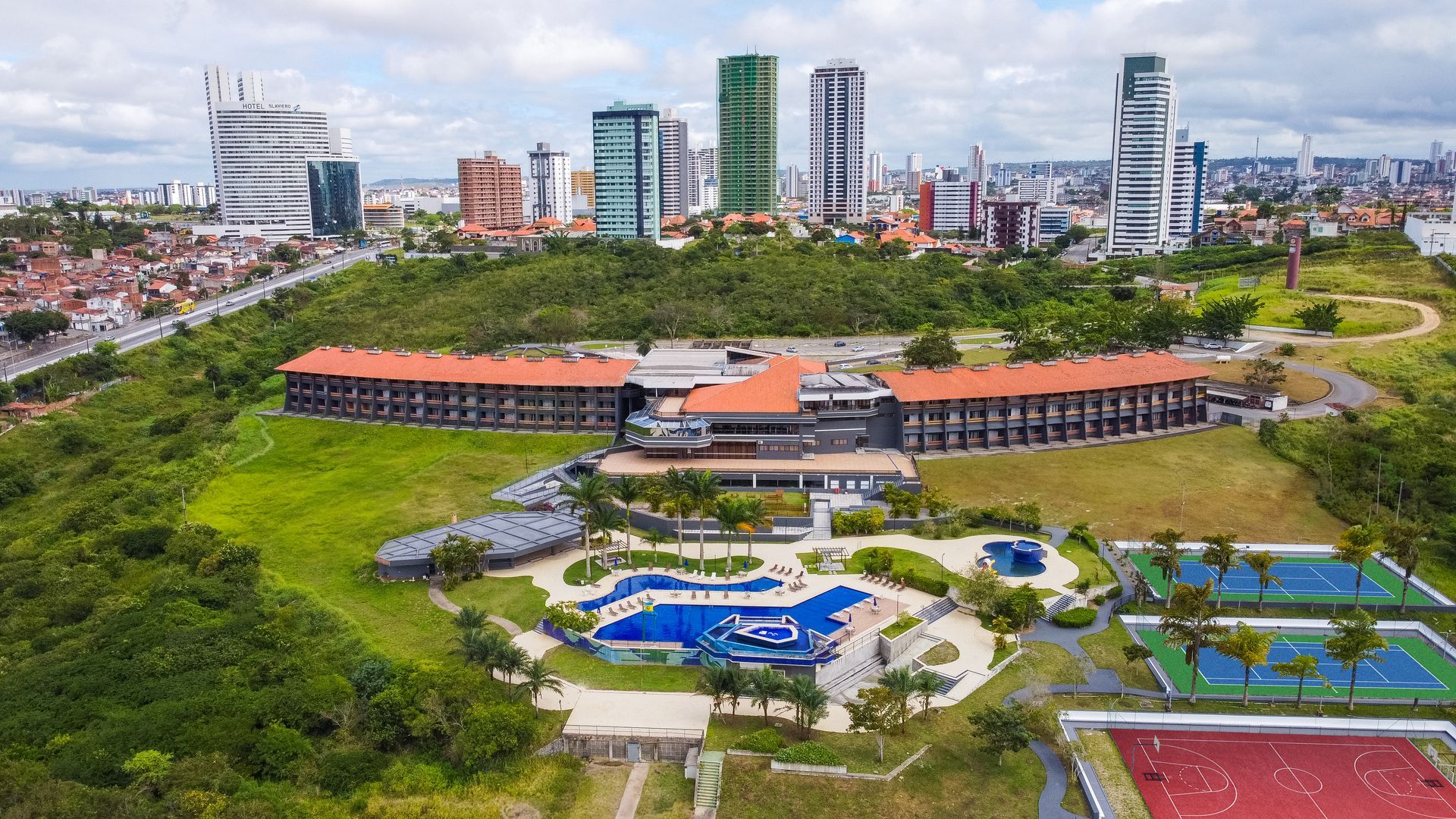 Uma vista aérea de um grande edifício com uma piscina em frente a uma cidade.