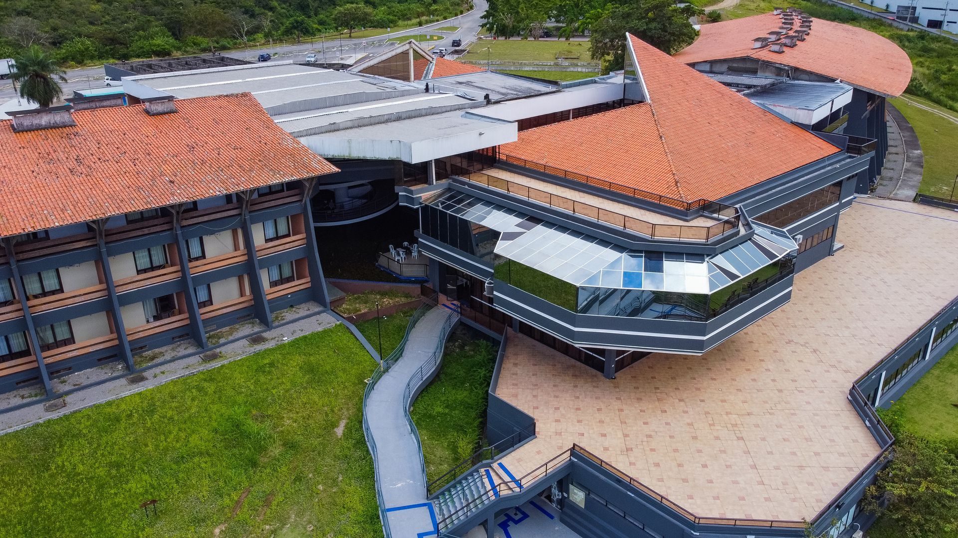 Uma vista aérea de um grande edifício com um telhado de telhas vermelhas cercado por grama e árvores.
