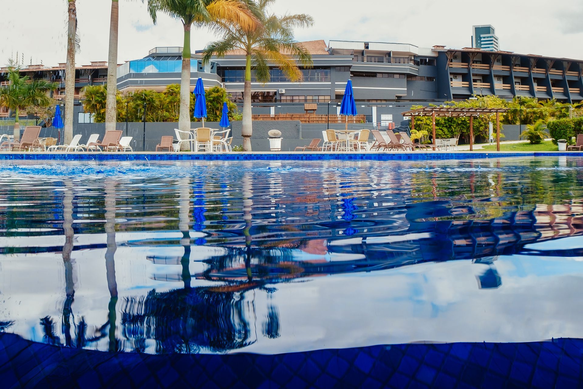 Uma grande piscina cercada por palmeiras e cadeiras com um prédio ao fundo.