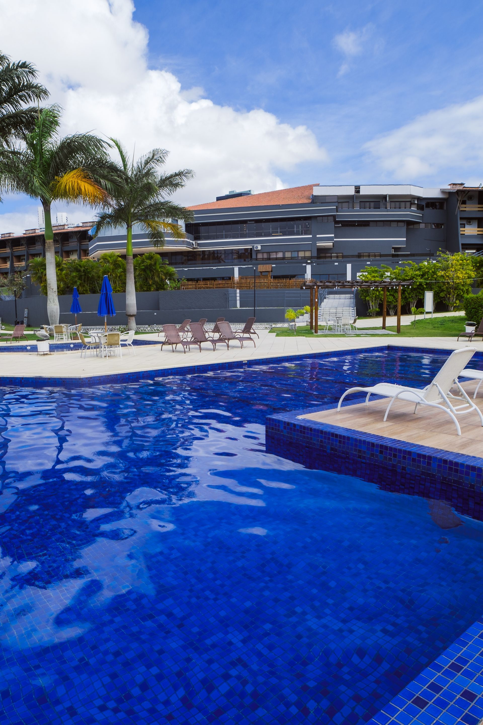 Uma grande piscina com cadeiras e guarda-sóis em frente a um prédio.