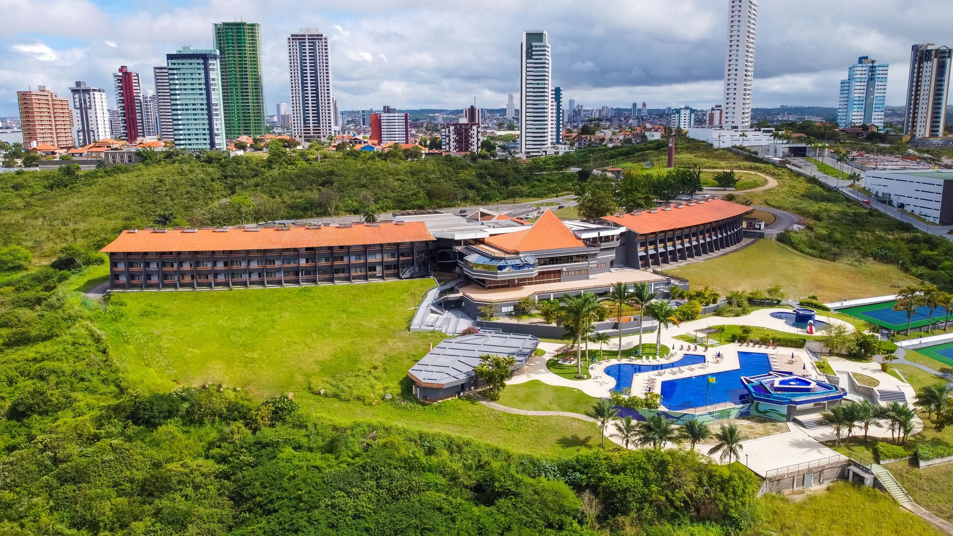 Uma vista aérea de um grande edifício com uma piscina em frente a uma cidade.