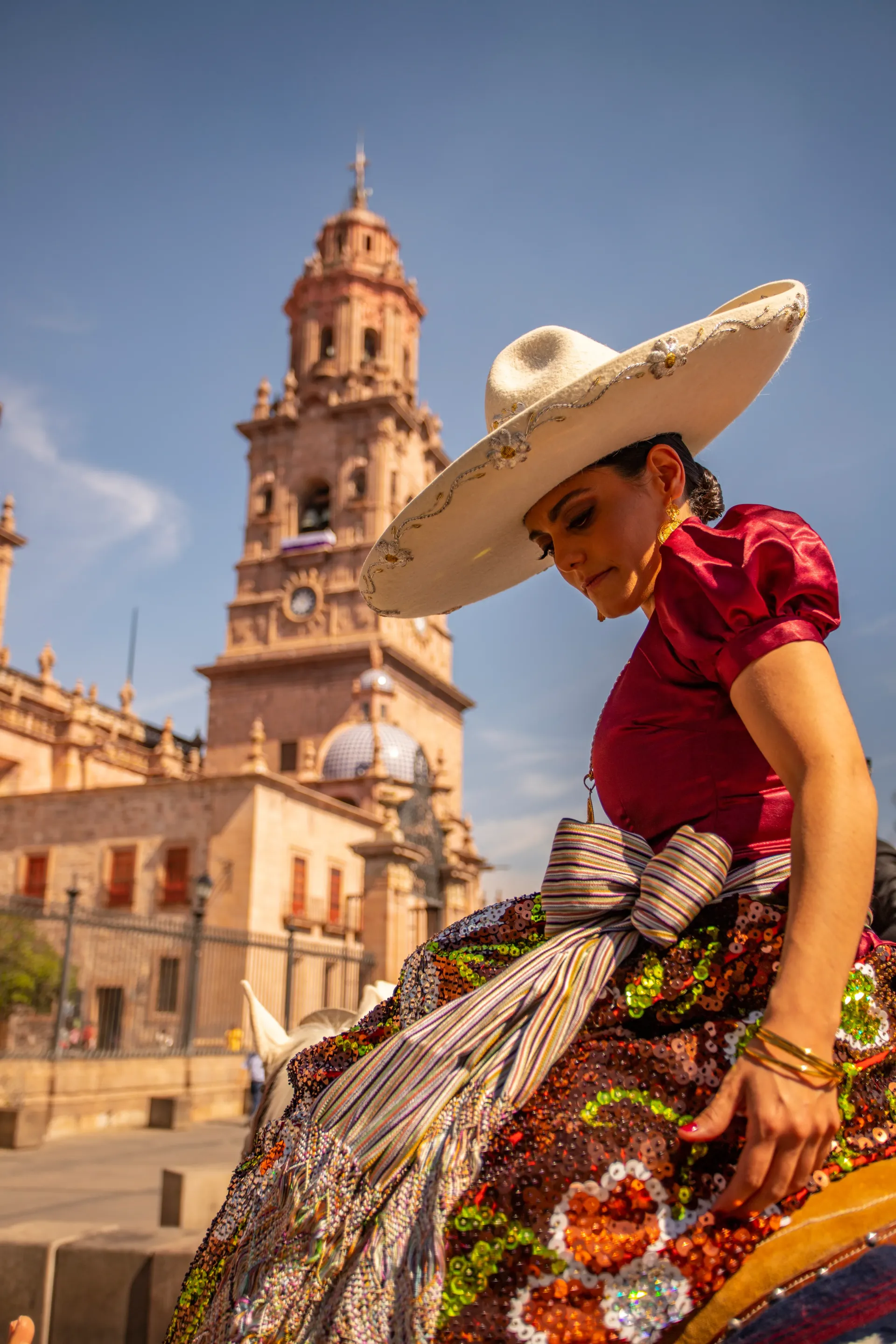 Una mujer que lleva un sombrero y un vestido está sentada frente a un edificio.