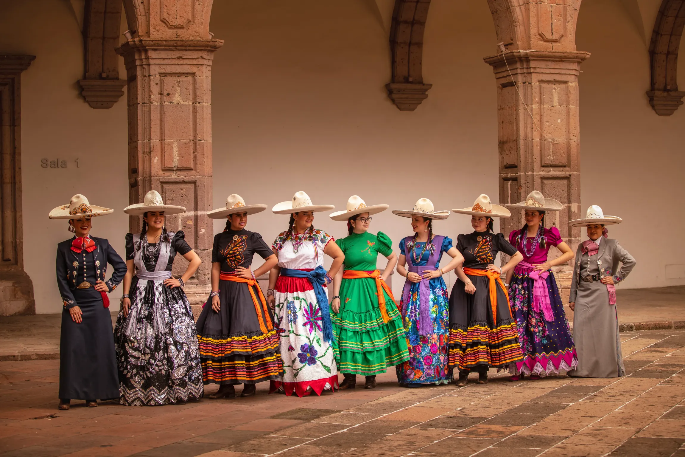 Un grupo de mujeres con vestidos y sombreros tradicionales mexicanos están de pie en una fila.