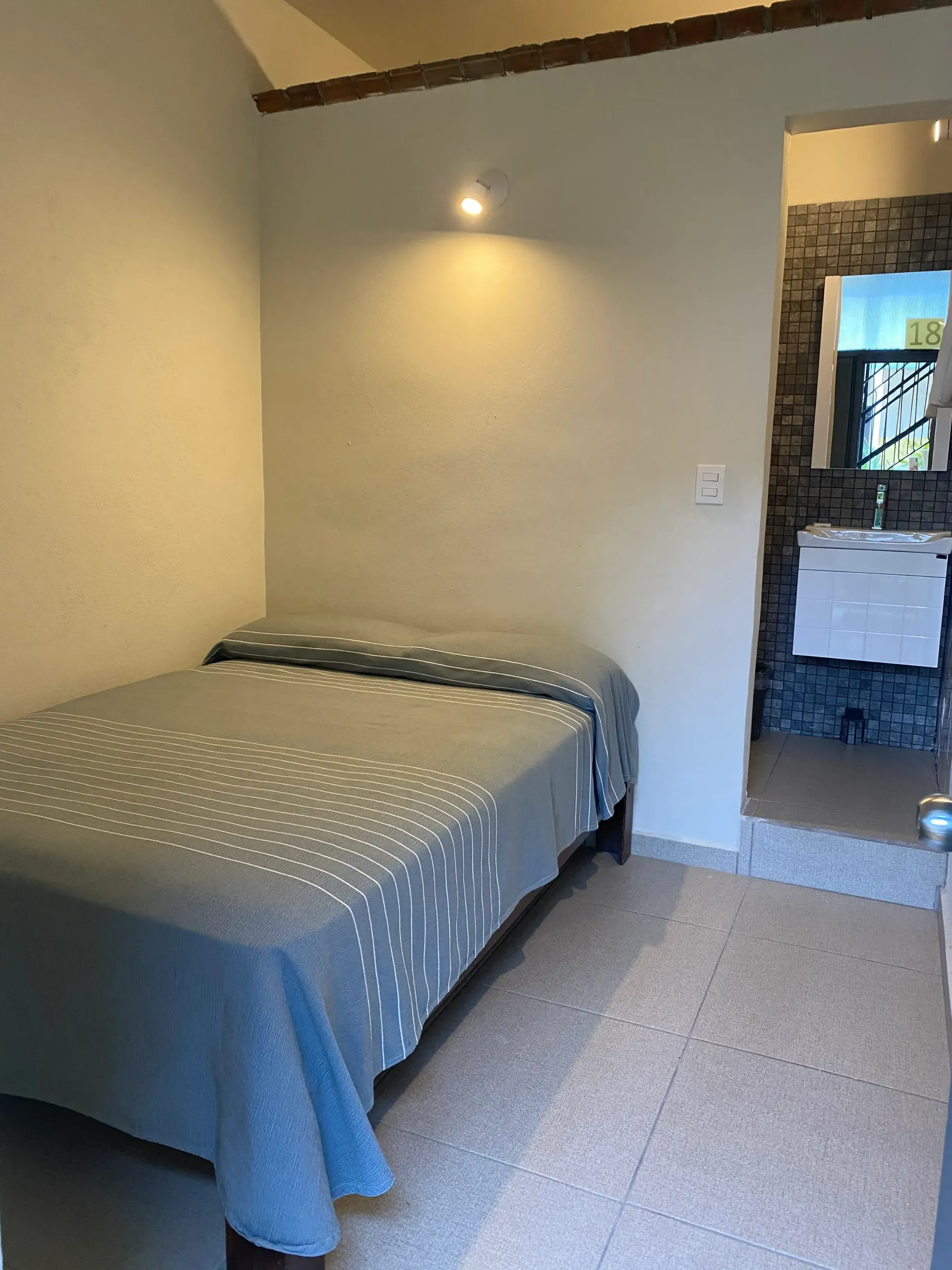 A bedroom with a bed and a bathroom in the background.