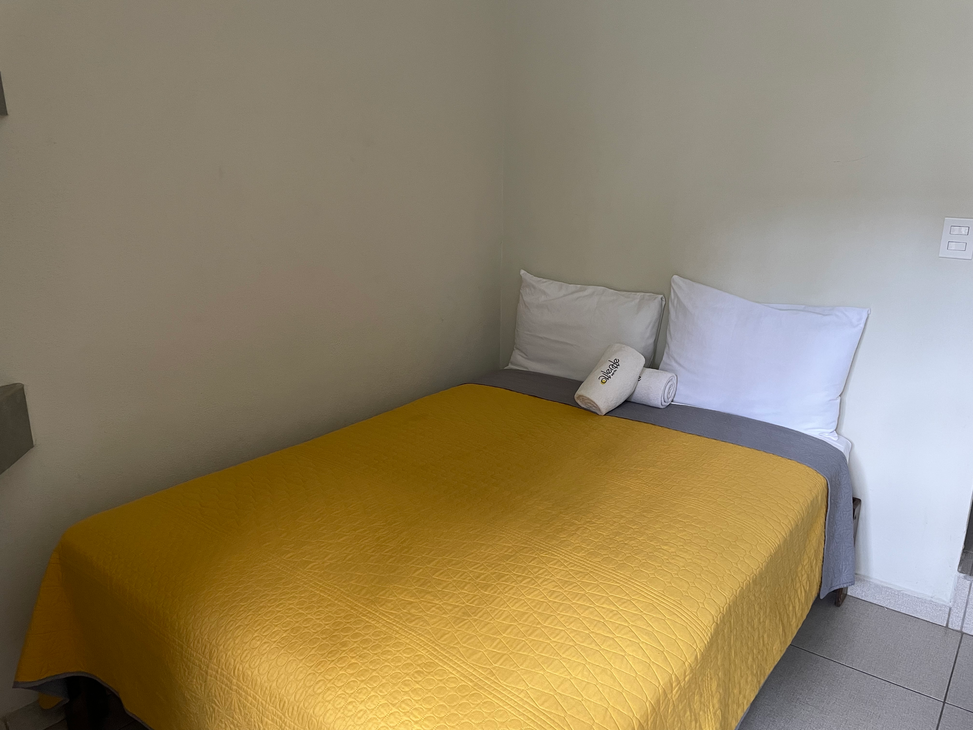 A bed with a yellow blanket and white pillows in a small room.