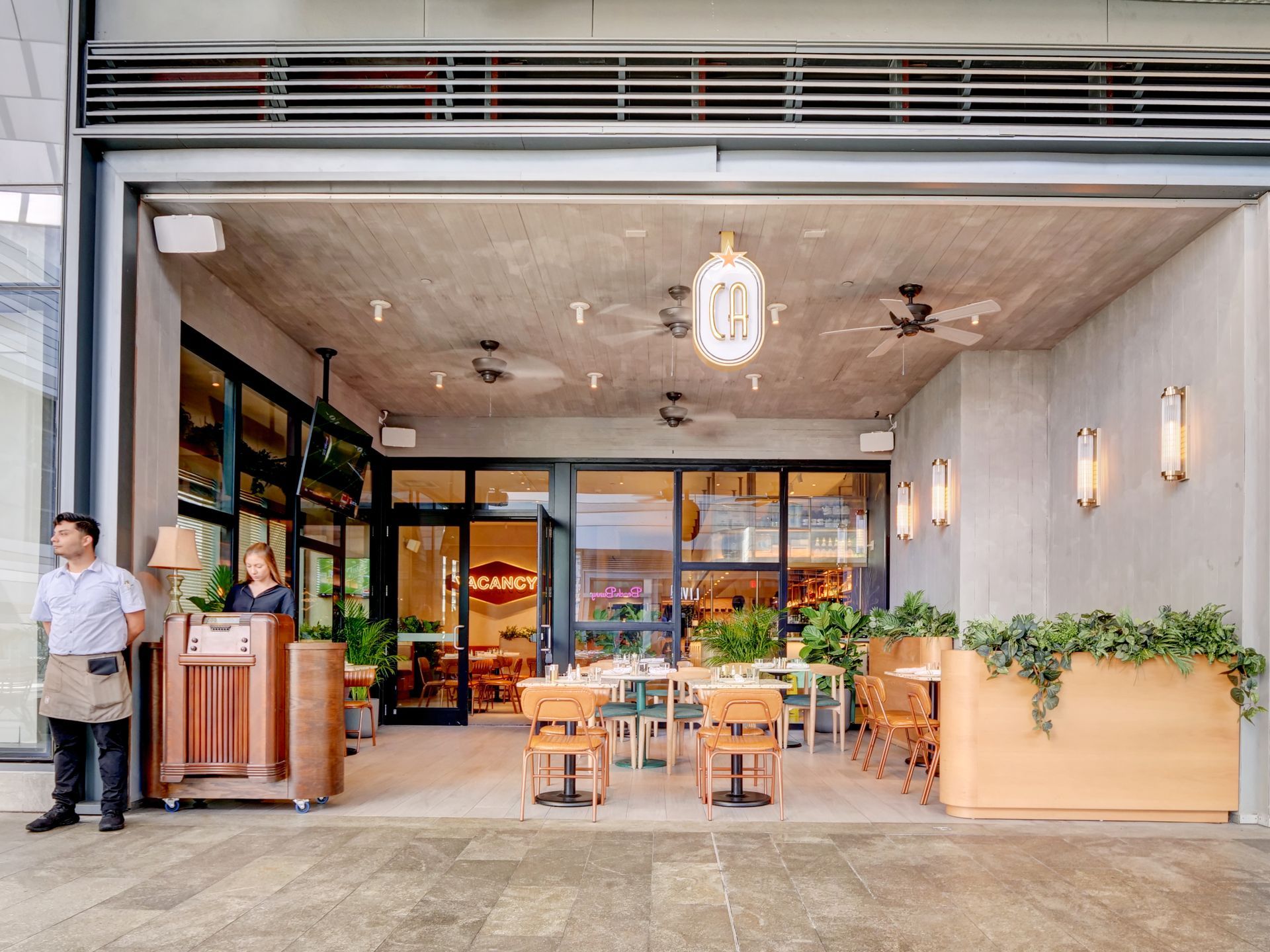A man is standing in front of a restaurant with tables and chairs.