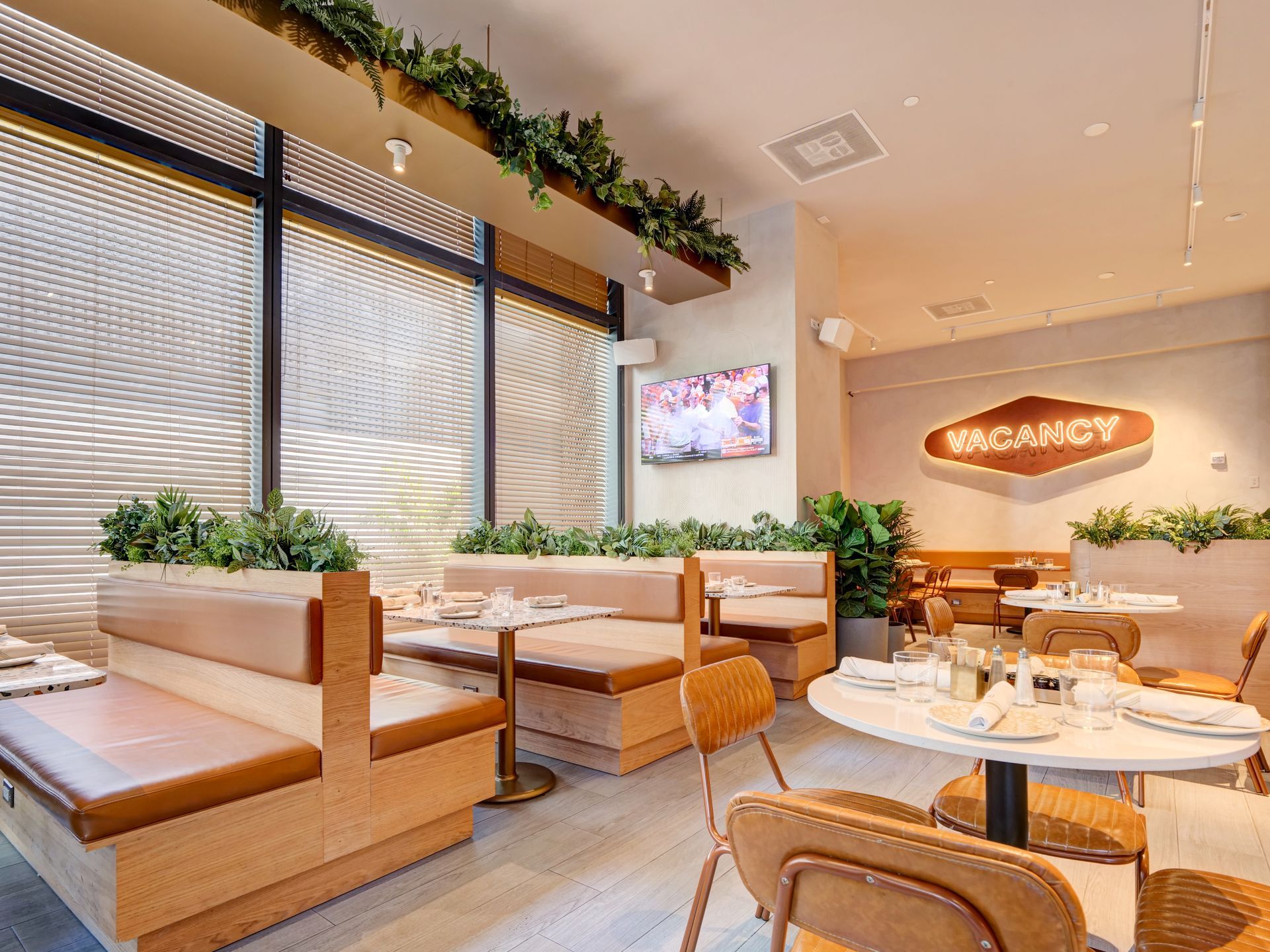 A restaurant with tables and benches and a tv on the wall.