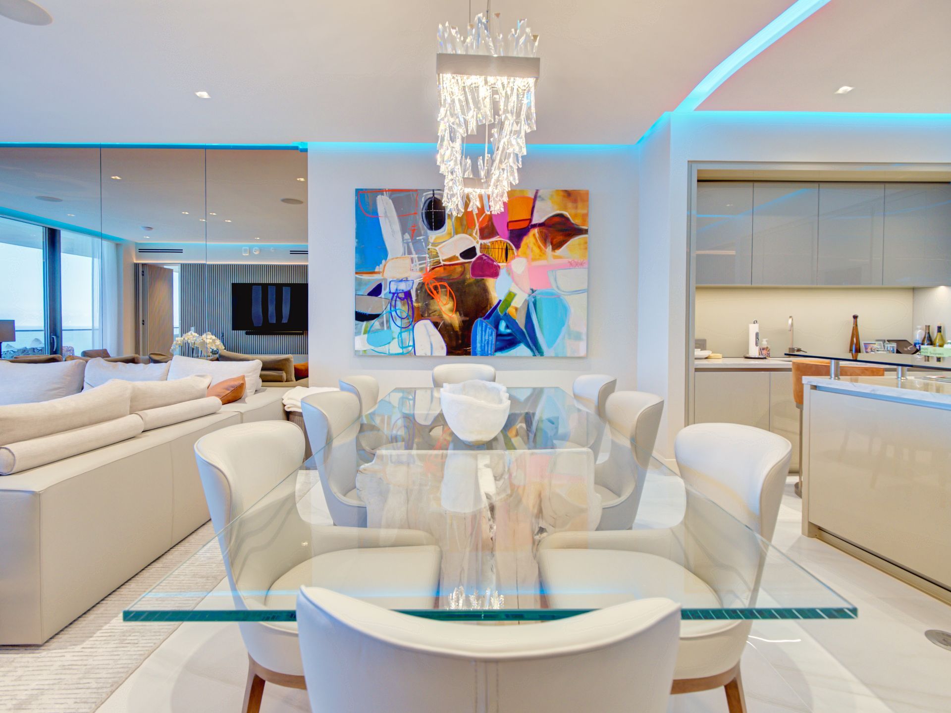 A dining room with a glass table and chairs and a painting on the wall.