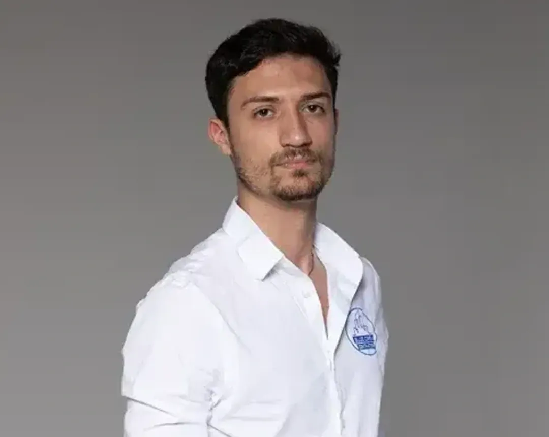 A man in a white shirt is standing in front of a gray background.