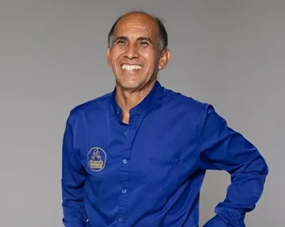 A man in a blue shirt is smiling with his hands in his pockets