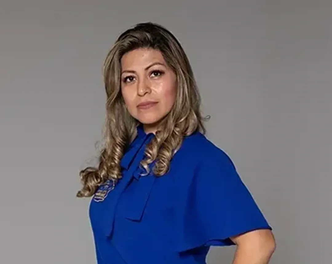 A woman in a blue dress is standing in front of a gray background.