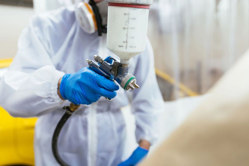 Operaio con tuta protettiva bianca spruzza del liquido con una pistola a spruzzo in un ambiente industriale.