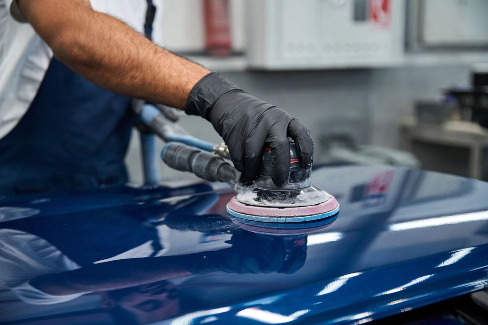 Una persona lucida il cofano di un'auto blu con una lucidatrice in un'officina.