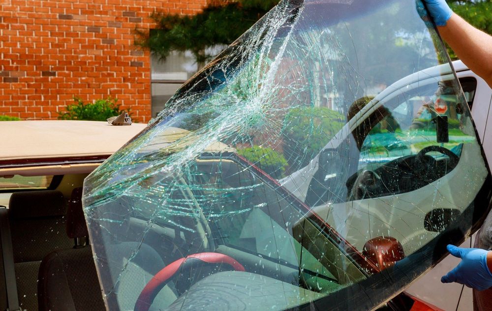 Una persona con guanti blu rimuove all'aperto il parabrezza di un'auto in frantumi.