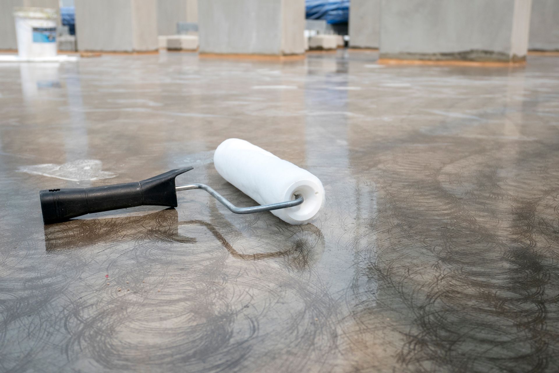 A paint roller on a wet, gray concrete floor.