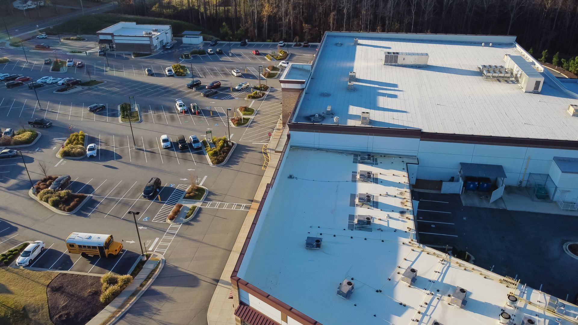 Aerial view of a commercial building with a large parking lot and several vehicles parked.