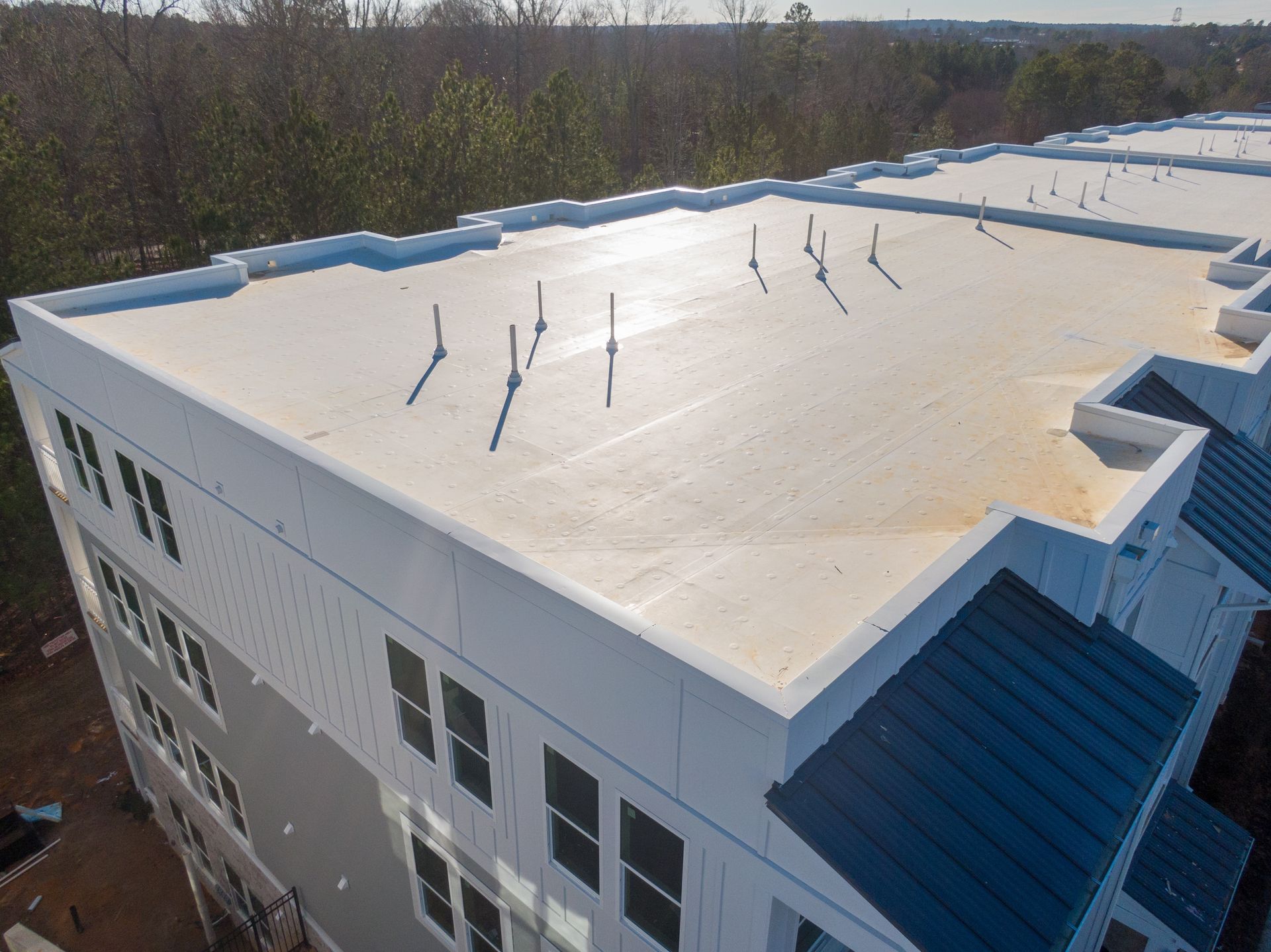 Overhead view of a white flat roof on a multi-story building, with several vertical pipes protruding.