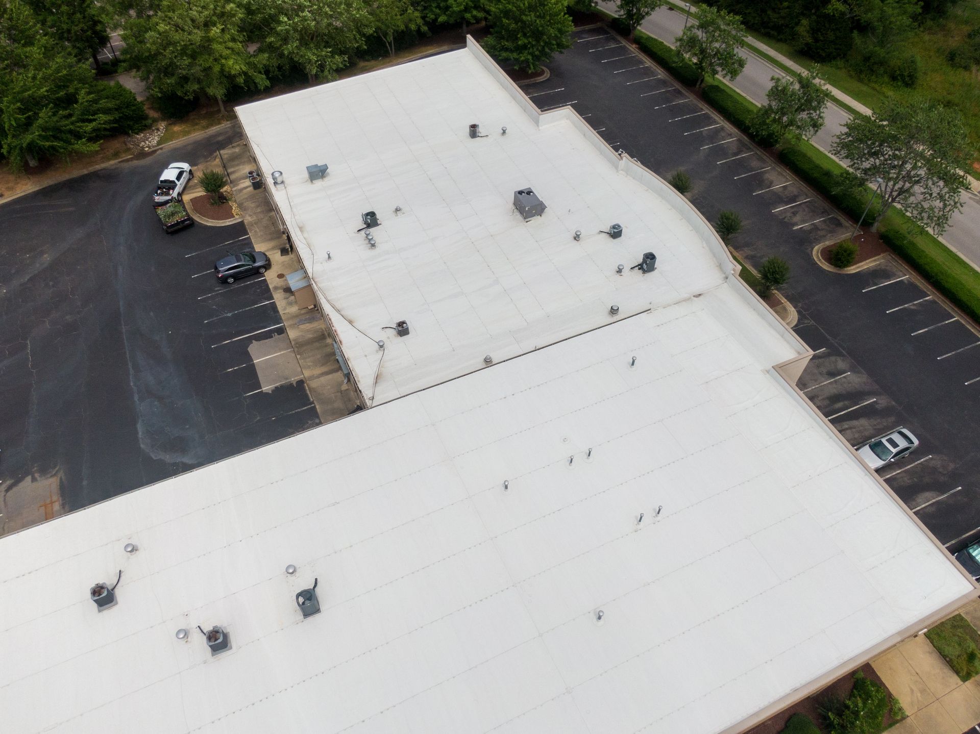 Aerial view of a white commercial roof with HVAC units. Parking lot and trees surround the building.