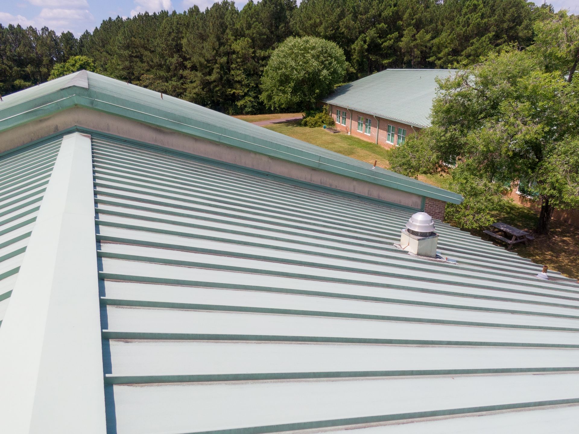 Green metal roof on a building, angled view, other buildings and trees in the background.