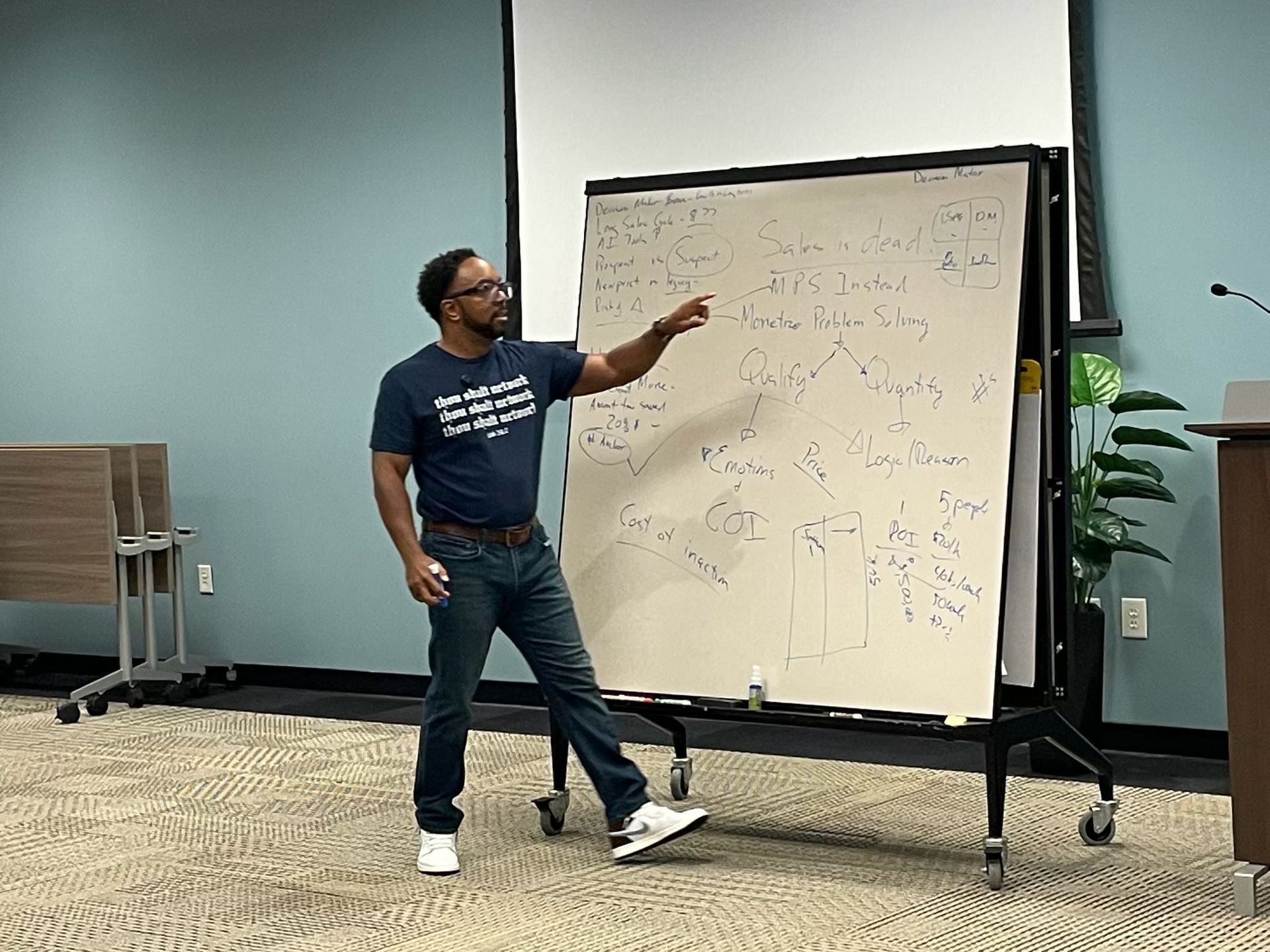 A man is standing in front of a whiteboard and pointing at it.