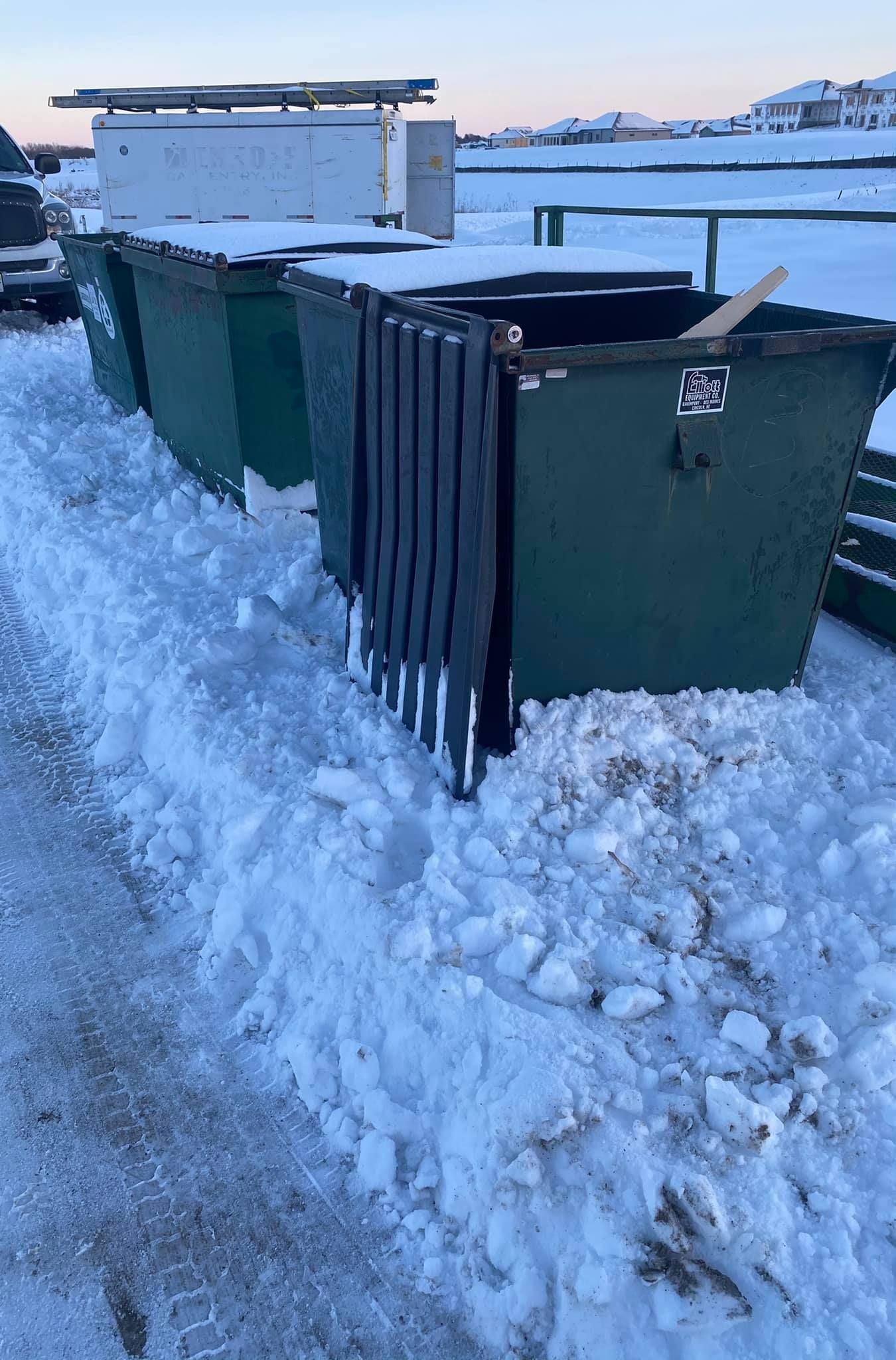 A green dumpster is sitting in the middle of a snowy field.