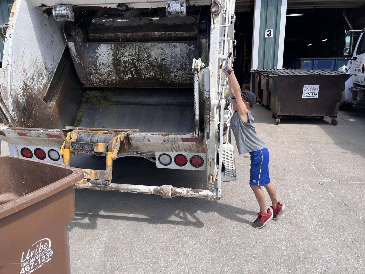 A young boy is standing in front of a garbage truck.