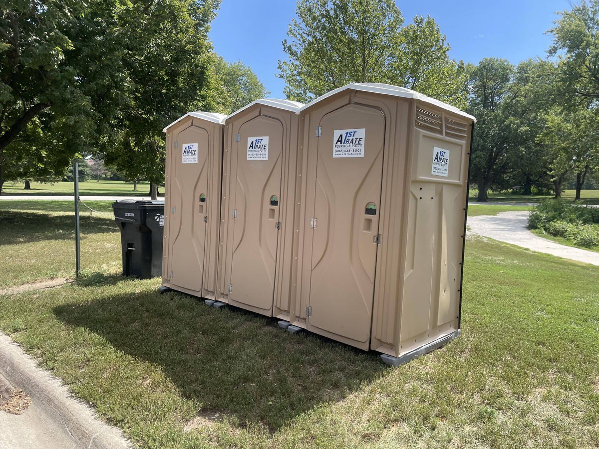 Three portable toilets are lined up next to each other in a park.