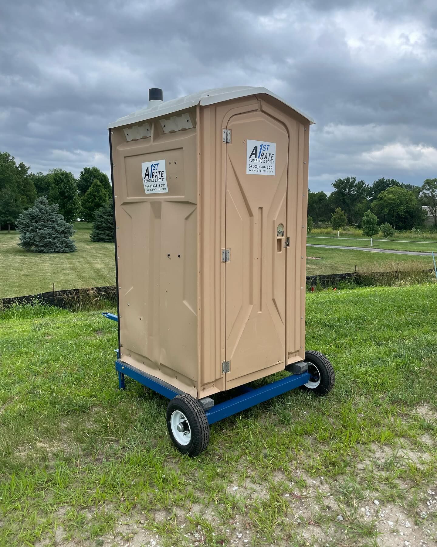 A portable toilet is sitting on a cart in a grassy field.