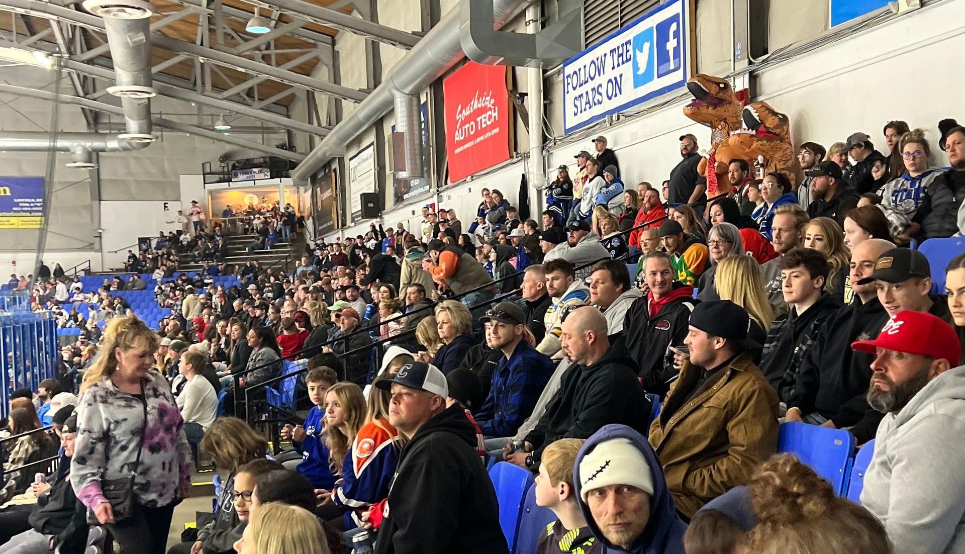 A large crowd of people are sitting in a stadium watching a hockey game.