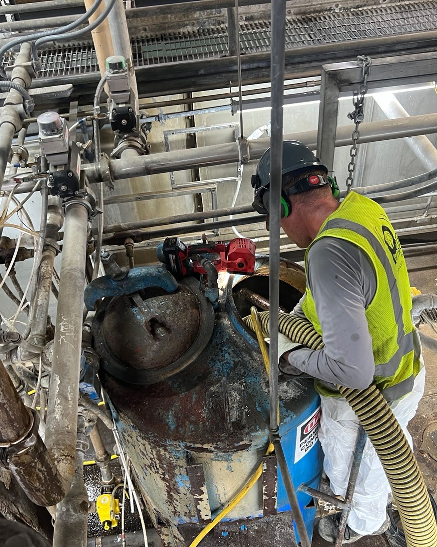 A man in a yellow vest is working on a machine in a factory.