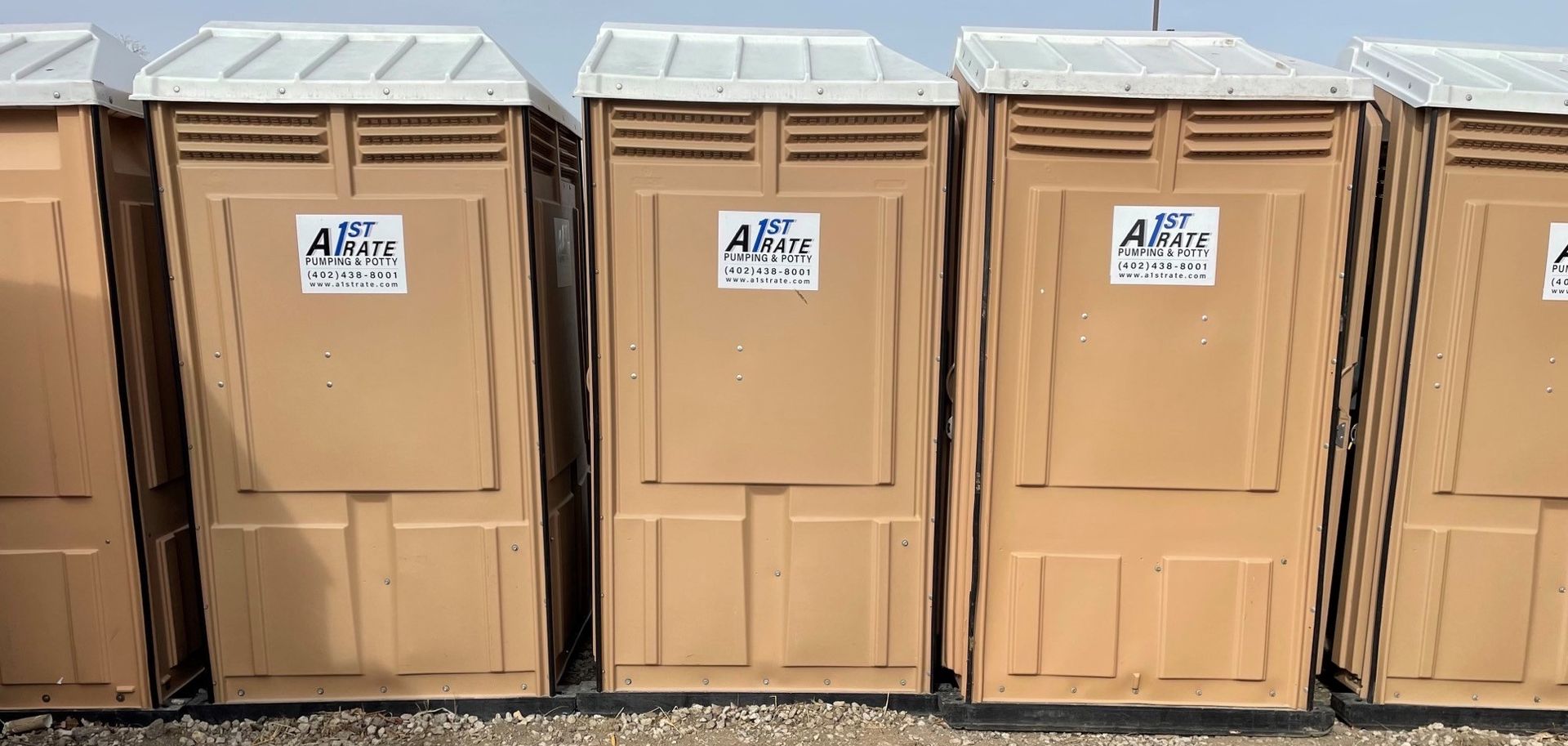A row of brown portable toilets are lined up in a row.