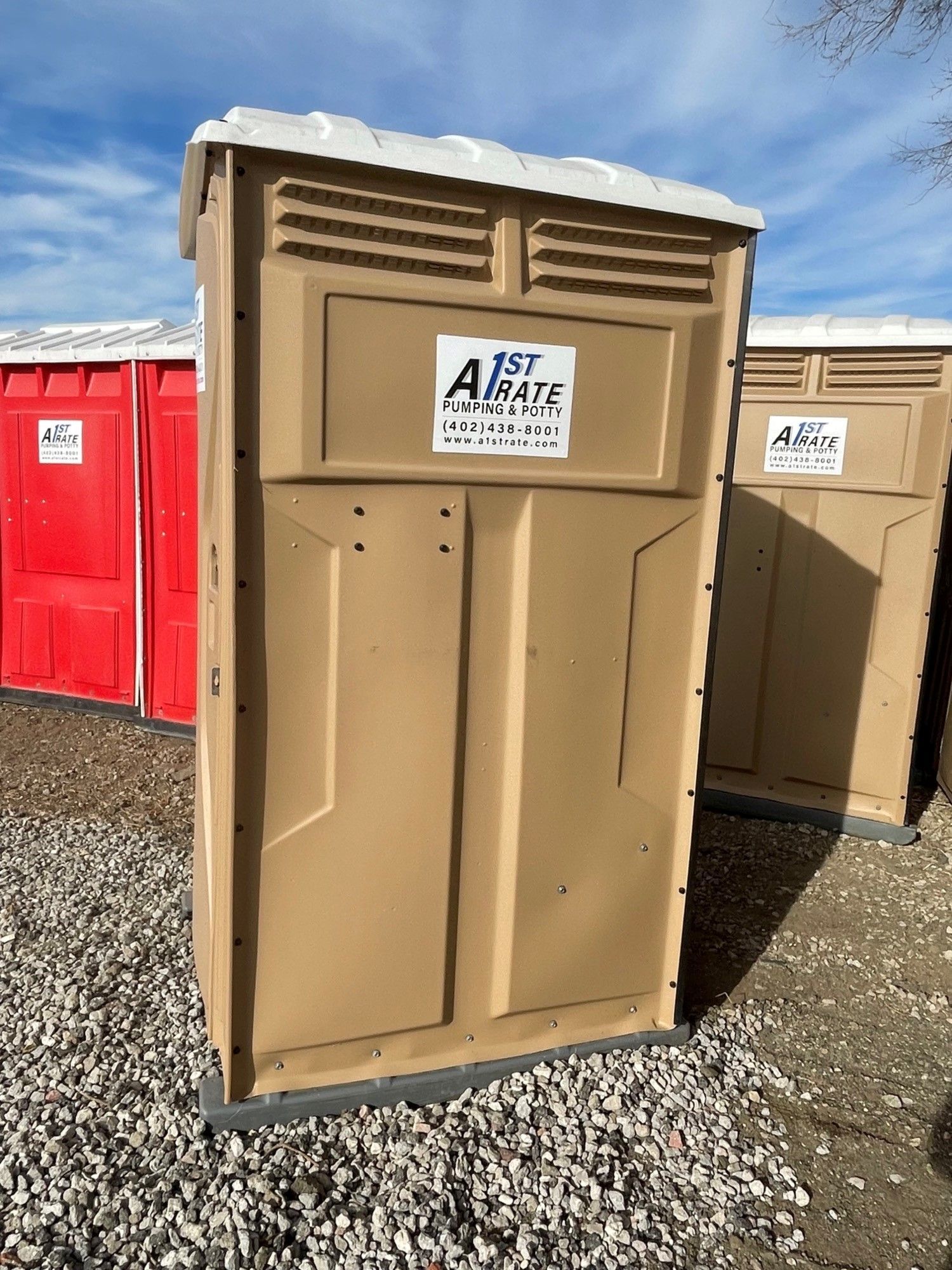 A brown portable toilet is sitting in a gravel area.