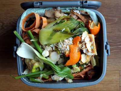 A trash can filled with food scraps and vegetables on a wooden table.