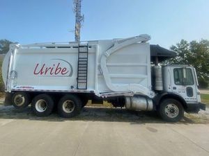 A white garbage truck is parked on the side of the road.